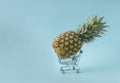 Creative concept of fresh pineapple in a smal shopping basket ot cart. Pastel blue background
