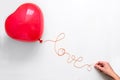 Creative concept. Hand holding red heart shape balloon with Love word from thread on white wooden background. Flat lay. Top view. Royalty Free Stock Photo