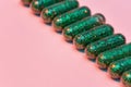 Creative concept with many green glitter pills lying diagonally in a row isolated on pastel pink background. Minimal Royalty Free Stock Photo