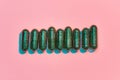 Creative concept with many green glitter pills lying in a row horizontally isolated on pastel pink background. Minimal Royalty Free Stock Photo