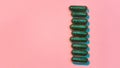 Creative concept with many green glitter pills lying in a row vertically isolated on pastel pink background. Minimal Royalty Free Stock Photo