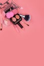 Creative concept with shopping trolley with makeup on a pink background. Perfume, sponge, brush, mascara, eye shadow, lip gloss in