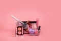 Creative concept with shopping trolley with makeup on a pink background. Perfume, sponge, brush, mascara, eye shadow, lip gloss in