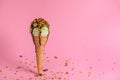 Creative concept with unstable pistachio ice cream cone with chocolate sauce and strewed nuts on pink background Royalty Free Stock Photo