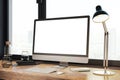 Creative designer desk with empty white computer monitor, lamp, supplies and other items. Window with city view in the background Royalty Free Stock Photo