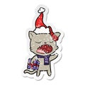 A creative distressed sticker cartoon of a cat with christmas present wearing santa hat