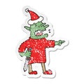 A creative distressed sticker cartoon of a goblin with knife wearing santa hat
