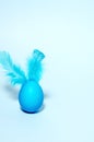 Creative easter bunny - blue egg and ears of feathers stands on a blue background. Monochrome, minimalistic background.