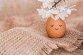 Creative easter egg in floral wreath, cute face and sleepy eyes on sackcloth background. Happy Easter concept Royalty Free Stock Photo