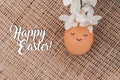 Creative easter egg in floral wreath, cute face and sleepy eyes on sackcloth background. Happy Easter concept Royalty Free Stock Photo