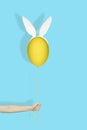 Creative easter minimal concept. Hand holding a yellow egg in bunny ears like balloon on a string on light blue background