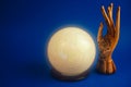 Esoteric still life with a ball of predictions and wooden female hand on a vibrant blue background