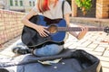 Creative female playing acoustic guitar sitting on sidewalk with guitar case and cash Royalty Free Stock Photo