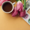 Creative flat lay of coffee cup, watercolor palette and bouquet of pink tulips. Artist workplace on a pale peach pastel background