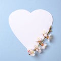 Creative flat lay composition: heart-shaped paper and blooming sakura branch on blue background. Top view, floral round frame,