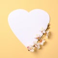 Creative flat lay composition: heart-shaped paper and blooming sakura branch on yellow background. Top view, floral frame,