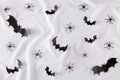 Creative flat lay Halloween background with bats silhouettes and spiders on white silk background.