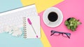 Top view office desk with notepad, wireless keyboard, succulent plant, coffee cup and glasses on pastel colored background.