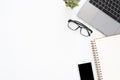 Top view office desk with laptop, glasses, phone, notebook and plant on white color background.