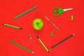 Creative flat lay of school supplies - green pens, pencils, scissors and an apple on a red background Royalty Free Stock Photo