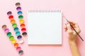 Creative flat lay of watercolor palettes, notebook, female hand holding paint brush. Artist workplace on a pink pastel background Royalty Free Stock Photo