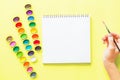 Creative flat lay of watercolor palettes, notebook, female hand holding paint brush. Artist workplace on a yellow background Royalty Free Stock Photo