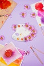 Creative flatlay with art supplies and white plastic artist palette with violet daisies.