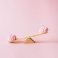 Creative food concept with a light wooden seesaw with pink cookies on it. Sweet and summer layout with a pastel pink background.