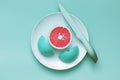 Creative food concept. Turquoise color grapefruit cut on a plate with a knife on turquoise background. Food art