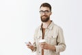 Creative good-looking and stylish businessman in glasses and beige jacket holding paper cup of coffee and smartphone Royalty Free Stock Photo
