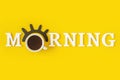 Creative good morning concept. White letters, black eyelashes, alarm clock and cup of coffee on yellow background. Top