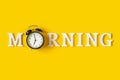 Creative good morning concept. White letters, black eyeleshes and alarm clock on yellow background. Top view, Flat lay