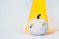 Creative Halloween background. Cute and shy pumpkin mummy with spider in yellow projector light beam on the white