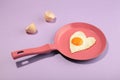 Creative idea with a pink frying pan and egg in heart shape on purple background. Minimal food and love concept. Breakfast idea