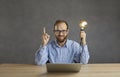 Happy man sitting at desk with laptop, holding idea light bulb and pointing finger up Royalty Free Stock Photo