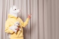 Creative lama person in yellow hoodie holding little white dog and pointing finger up on beige studio wall background