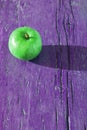 Creative layout with copy space, green juicy apple on vibrant violet shabby wooden background on hard sunbeams light with long sha