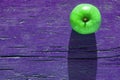 Creative layout with copy space, green juicy apple on vibrant violet shabby wooden background on hard sunbeams light