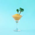 Creative layout made of martini glass, color sand and palm trees on blue background. Party drink concept. Royalty Free Stock Photo
