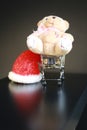 Red Christmas hat, coins in miniature of trolley and cute teddy bear toy isolated on black dark background Royalty Free Stock Photo