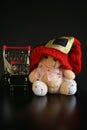 Red Christmas hat, coins in miniature of trolley and cute teddy bear toy isolated on black dark background Royalty Free Stock Photo