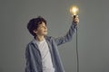 Creative little boy holding shining light bulb standing on gray studio background Royalty Free Stock Photo