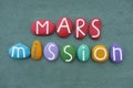 Mars Mission logo composed with multi colored stone letters over green sand