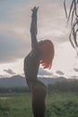 Creative look of woman in orange wig on green field over sunset