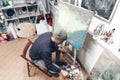 Creative man sits in a studio on a chair near a clean host, mixes a paint on a palette and paints a new painting. Top view.