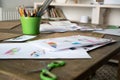 Pencils in a green plastic glass and paper with colored baby drawings are scattered on the work surface.