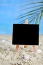 Creative minimal summer idea. Blackboard on sand with blur blue sea and tropical palm leaf. Vacation promotion sale concept. Creat Royalty Free Stock Photo