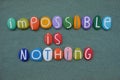 Impossible is nothing, motivational slogan composed with multicolored stone letters over green sand Royalty Free Stock Photo