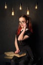 Creative old-fashioned student reading book sitting with illuminated edison lamps on the background