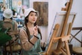 Creative painter painting in an art studio. Artistic young woman working on a new painting. Cheerful young artist looking at the